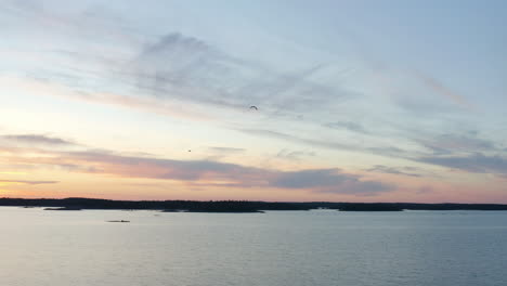 Vista-Aérea-De-Pájaros-Volando-Con-Un-Fondo-Colorido-Del-Cielo-Del-Atardecer,-En-La-Costa-De-Porkkalaniemi,-En-El-Archipiélago,-Soleado,-Atardecer-De-Verano,-En-Porkkala,-Golfo-De-Finlandia---Seguimiento,-Disparo-De-Drones