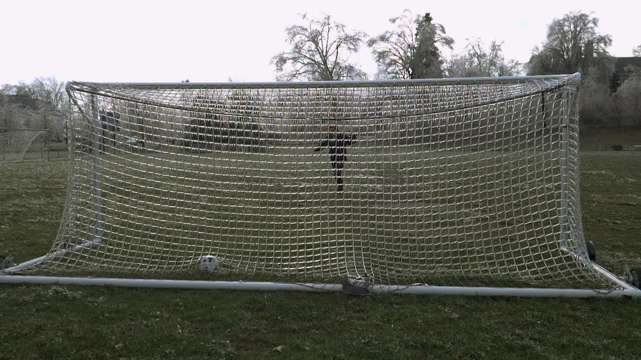 슬로우 모션: 한 남자가 축구공을 차서 축구 골대의 얼음 그물을 때리고 부서진 얼음을 공중으로 폭발시킵니다.