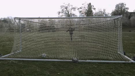 slow motion: a man kicks a soccer ball which slams an icy net of a soccer goal exploding shattered ice into the air