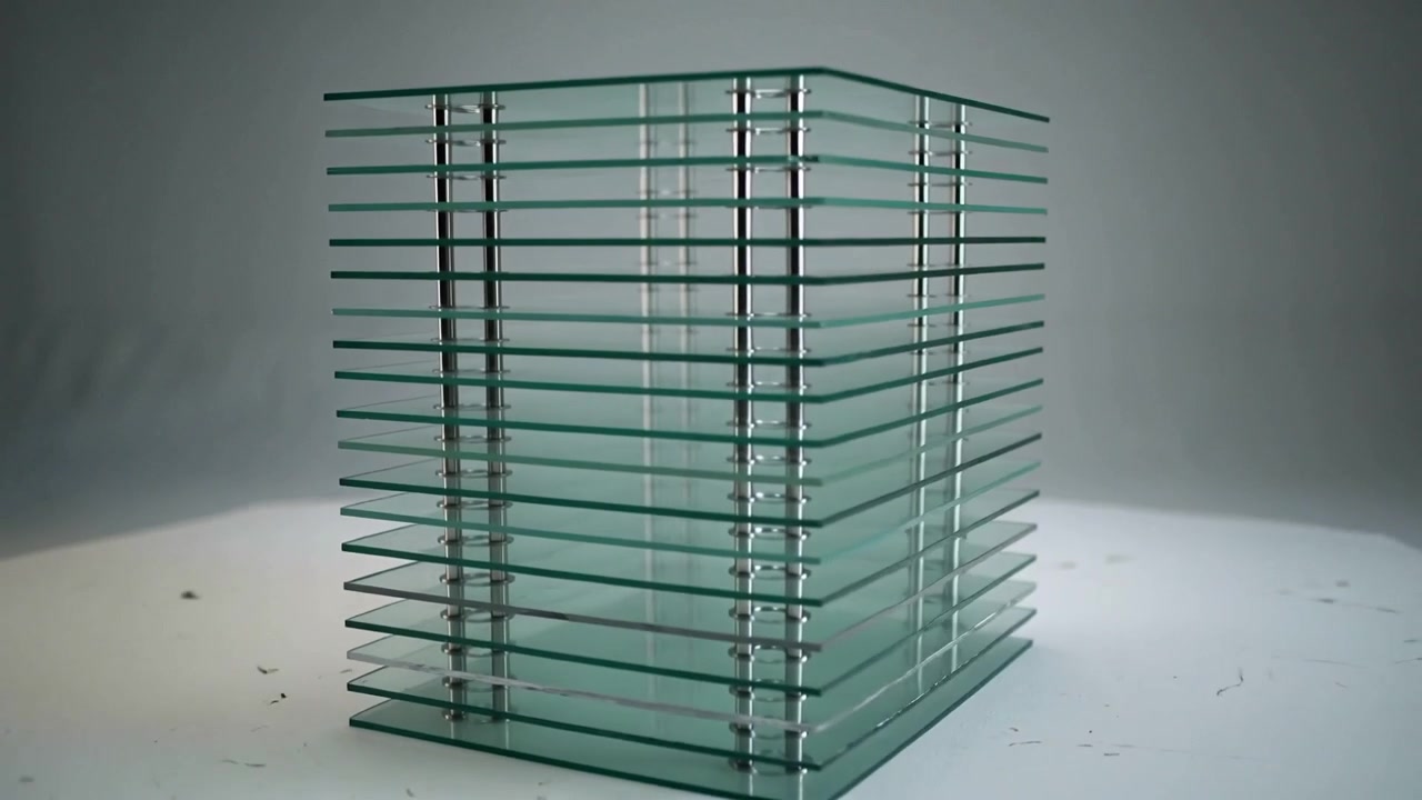 La cámara gira revelando un cubo de cristal apilado sobre una mesa de estudio, mostrando cuatro varillas espaciadoras de metal.