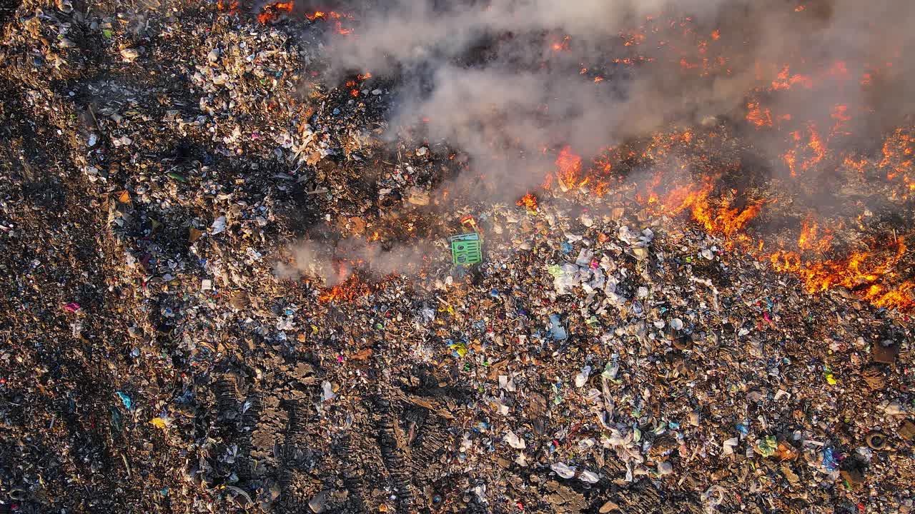 Raging fire spreads through landfill with dense smoke and visible waste piles