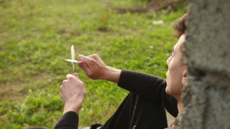 young man peeling stick with knife