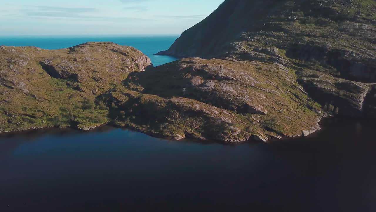 panorámica, inclinación hacia abajo, toma de drones de una colina rocosa sobre un lago en el sur de lofoten