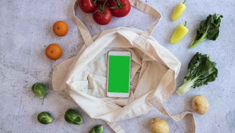 la recolección de productos veganos de comestibles en la bolsa reutilizable con la interfaz de pantalla verde del teléfono móvil en el diseño de colocación plana. compras en línea de verduras frescas y comercio electrónico. video de movimiento de parada