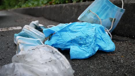 Dirty-discarded-used-corona-virus-masks-blowing-trash-in-wind-on-street-sidewalk-slow-closeup-dolly-left