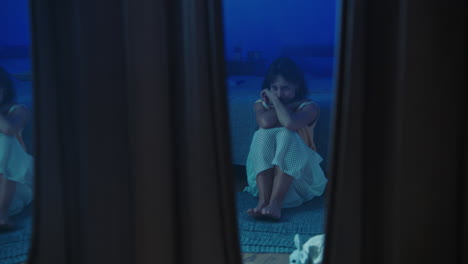a traumatised and disoriented girl sits on the bedroom floor
