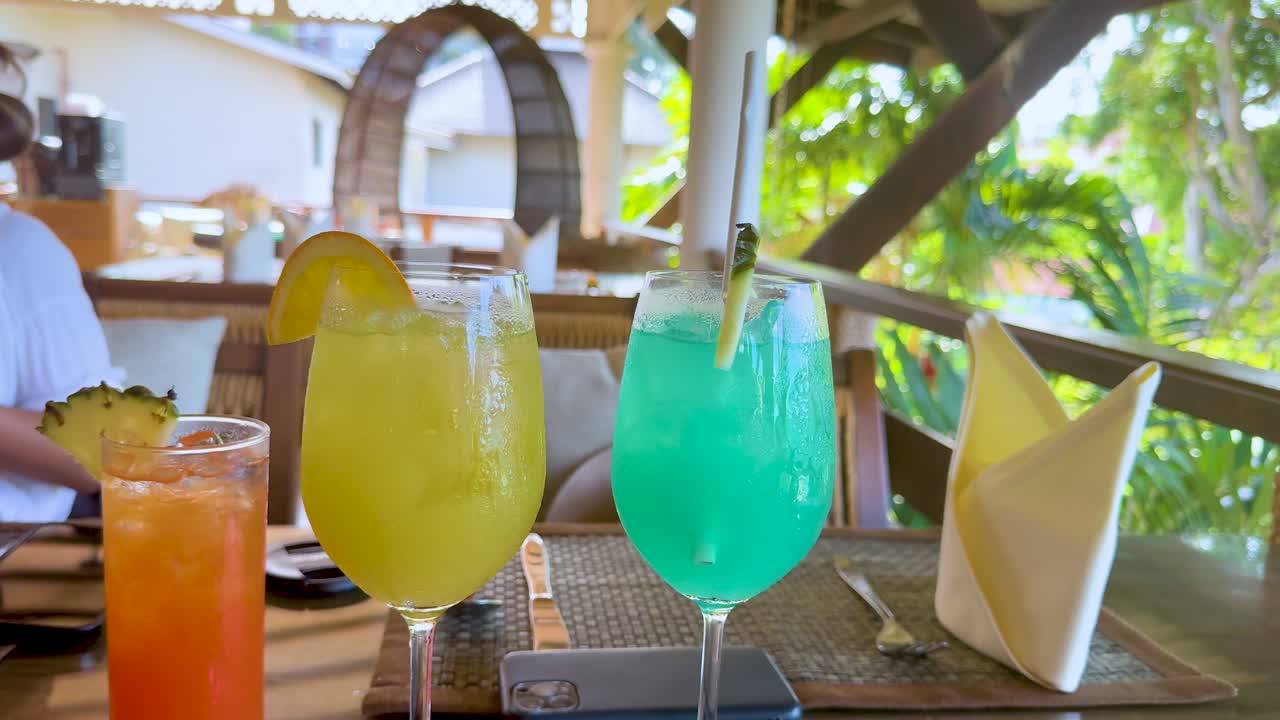 Three vibrant cocktails on a sunlit patio table, tropical setting, natural daylight, steady camera