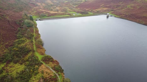 Drücken-Einer-Luftdrohne,-Die-über-Den-Lliw-Stausee-Mit-Pfad-Und-Kleinen-Gebäuden-Mit-Wasser-Geschossen-Wird,-Das-Zum-Unteren-Stausee-Hinunterfließt-4k