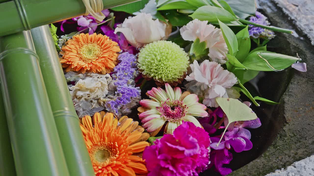 A close-up of a traditional stone purification basin (Temizuya) overflowing with colorful, floating flowers