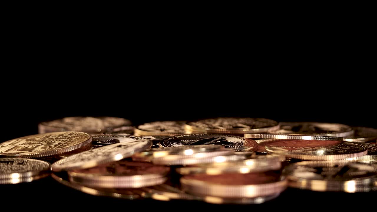 Gold-colored digital currency tokens fall onto a stack, dramatic lighting, slow-motion, black background
