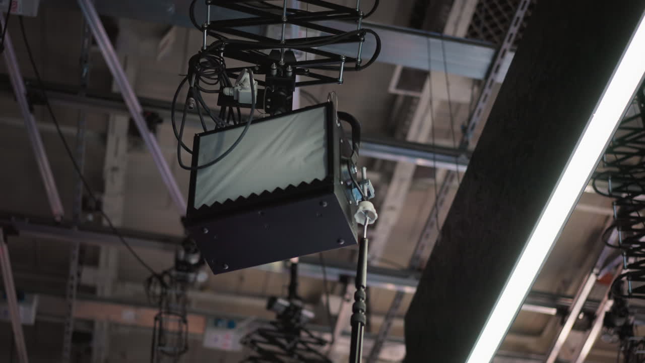 Overhead view of stage lighting in broadcast studio. Lighting equipment hanging from ceiling, adjusted by technician using boom pole to set up production for filming