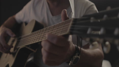 man playing acoustic guitar with black background and soft warm light