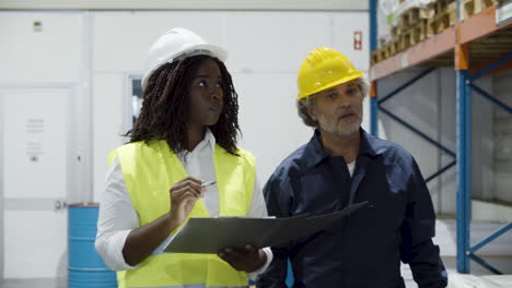 trabajadores multiétnicos en casco caminando y contando bienes en stock