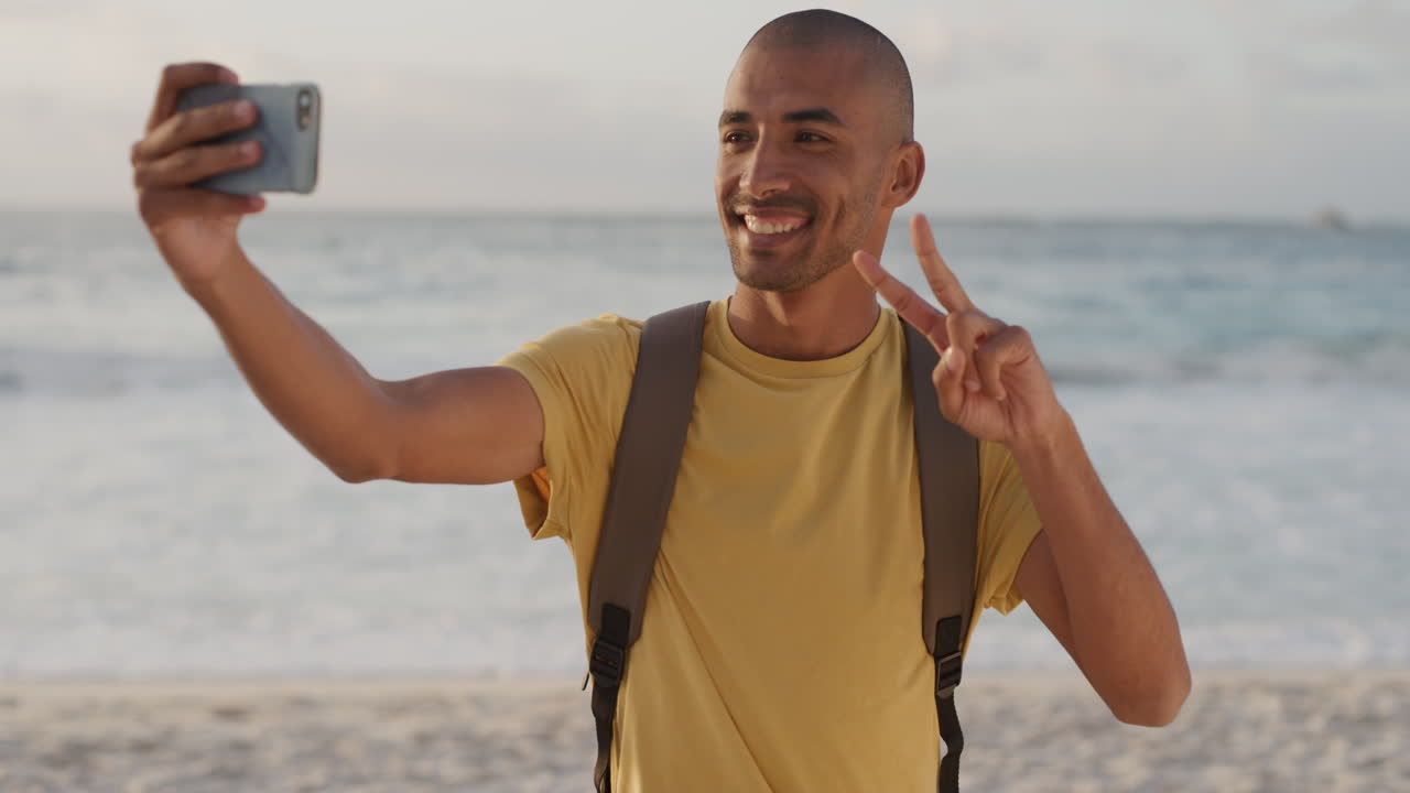 joven hispano usando un teléfono inteligente tomando una foto selfie en la playa disfrutando de un cálido día de verano compartiendo experiencia de vacaciones