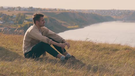 frustrated guy in jeans and pullover sits on river bank