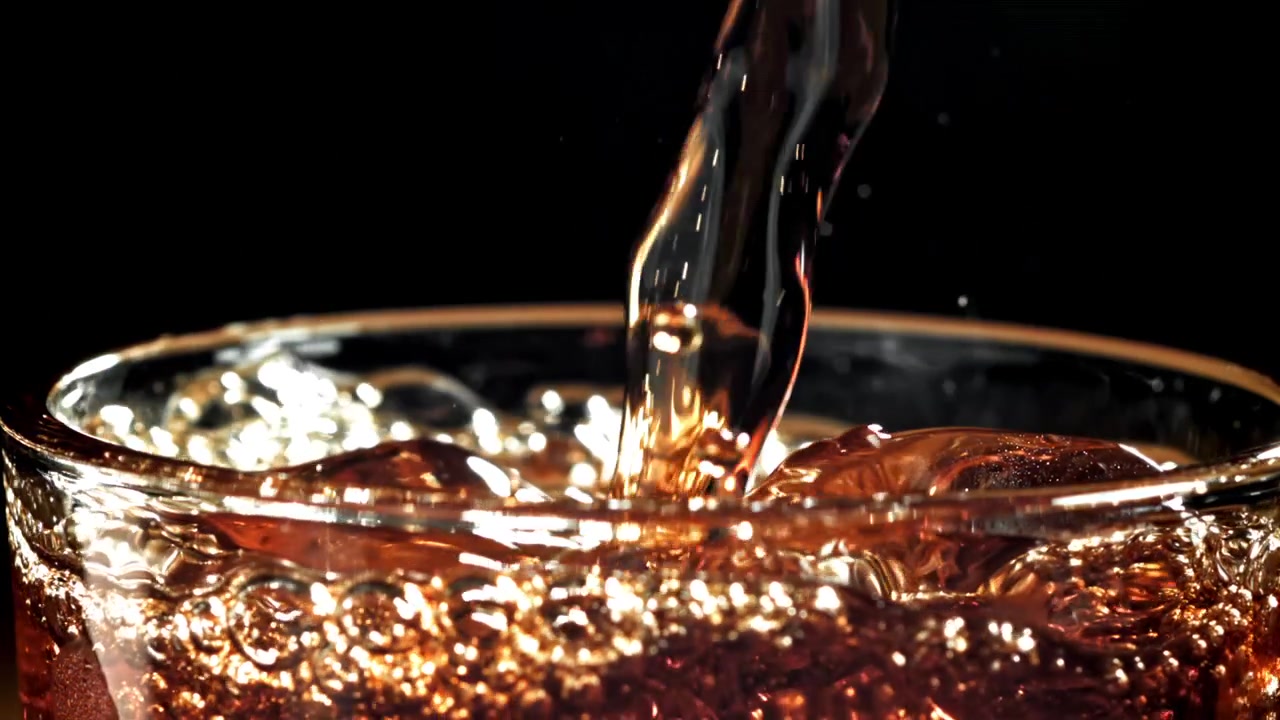 Rinfrescante bevanda ambrata versata in un bicchiere con ghiaccio al rallentatore