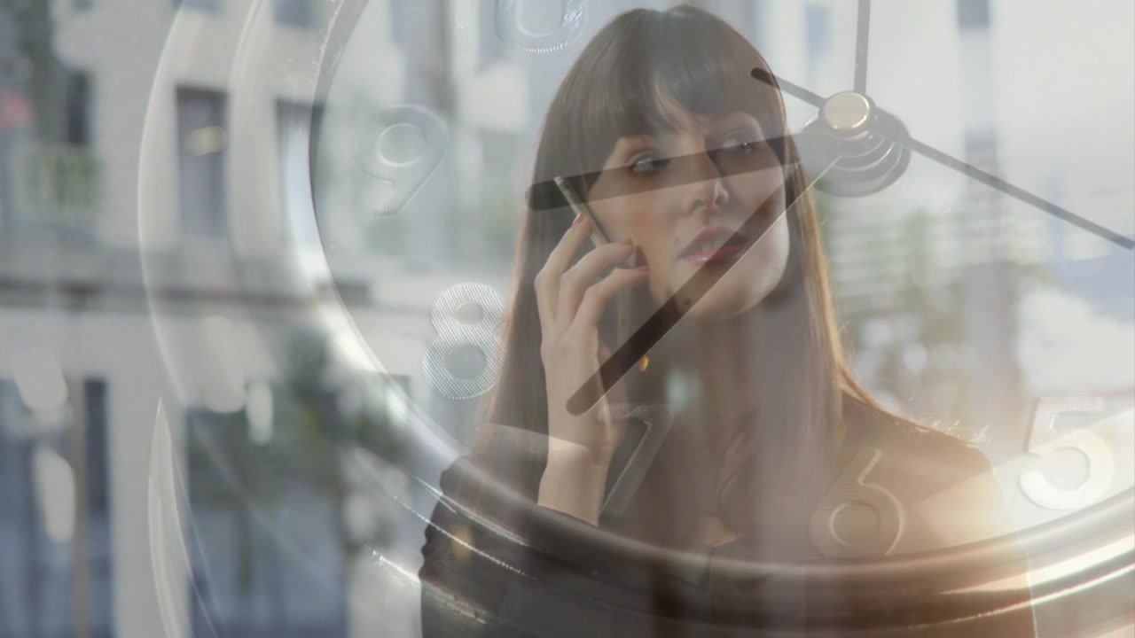 オフィスのアトリウムで着信に応答し、時計のオーバーレイ表示がある中でビジネスの電話対応をする女性。
