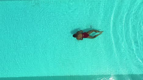 Mujer-En-Traje-De-Baño-Rojo-Realizando-Braza-Submarina-En-La-Piscina-Bali-De-La-Playa-Perenenan,-Vista-Aérea-Superior-Tiro-De-Elevación