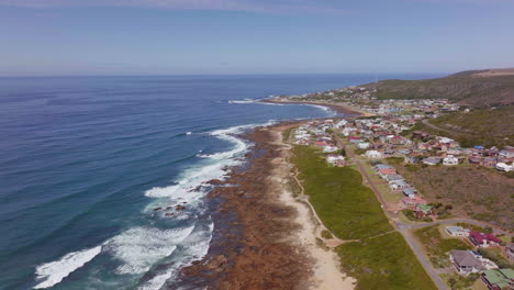 Still-Bay-aerial-drone-cinematic-beach-small-surf-town-Garden-Route-South-Africa-Jeffreys-Bay-homes-and-buildings-waves-crashing-on-reef-late-morning-afternoon-forward-movement