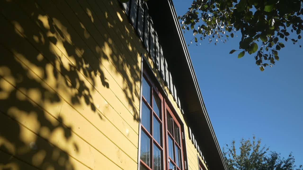Low angle view on wooden yellow house with shadow of swaying leaves