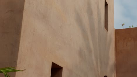 close-up shot of geometric building facade with palm tree shadow cast by bright sun in marrakech, morocco, highlighting contrast and texture
