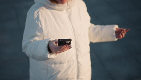 Dancer strolling through video checking phone while spinning under warm sunset sky wearing puffer coat and beanie against snowy pavement and forest backdrop capturing graceful motion and joyful vibe
