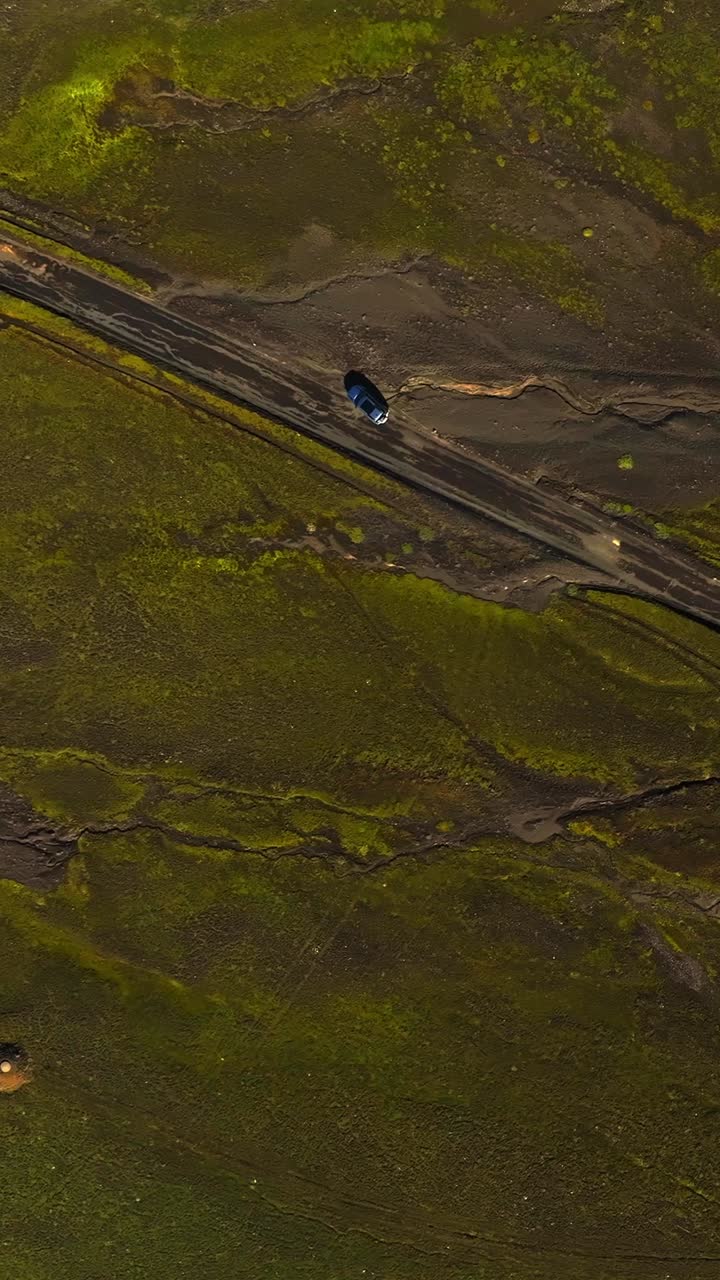 Ripresa aerea verticale dall'alto di un SUV che percorre una strada sterrata attraverso gli altopiani islandesi ricoperti di muschio, attraversando un terreno vulcanico e una tundra remota