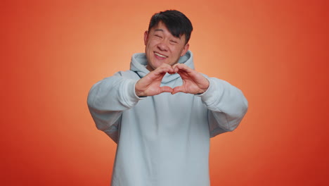 Smiling-chinese-man-makes-heart-gesture-demonstrates-love-sign-expresses-good-feelings-and-sympathy