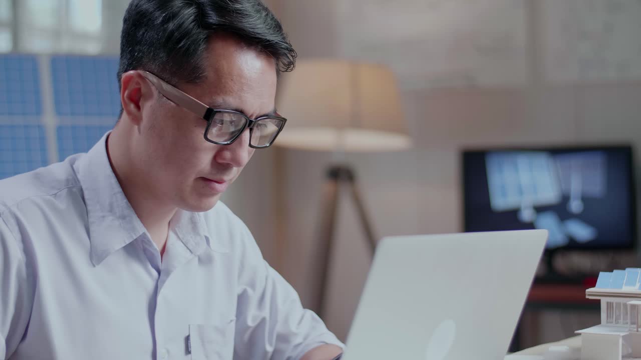 사무실에서 태양광 패널과 풍력 터빈을 가진 작은 집의 모델 에 노트북에서 타이핑하는 아시아 남자의 클로즈업