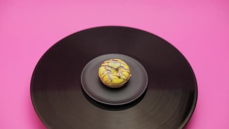 an american donut topped with yellow chocolate with blue and black choco lines turns in a circle on a black turntable. the shot from above