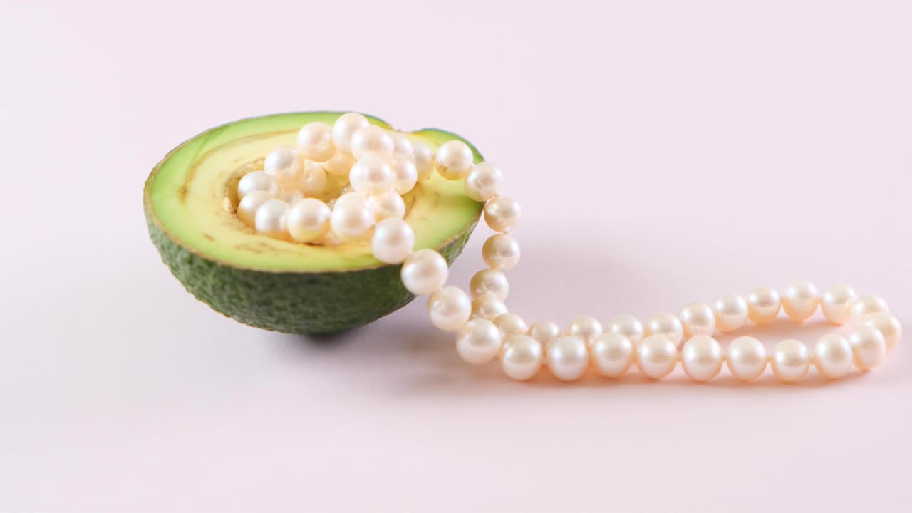 la mitad de un aguacate con perlas en un fondo rosa claro. surrealismo. diseño de alimentos de moda
