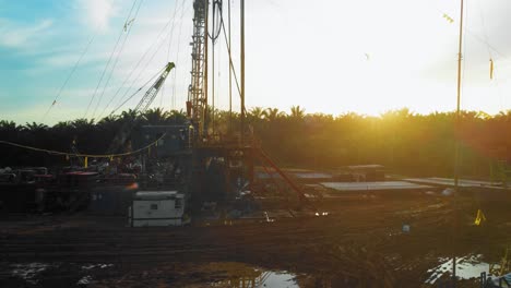 Cinematic-4K-Drone-Footage-of-Onshore-Drilling-Rig-equipment-structure-for-oil-exploration-and-exploitation-in-the-middle-of-jungle-surrounded-by-palm-oil-trees-during-sunset-and-high-oil-price