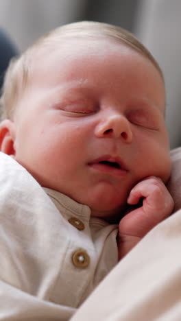 sweet newborn baby holding a hand near the cheek while sleeping. infant resting in mom's hands. close up. vertical video