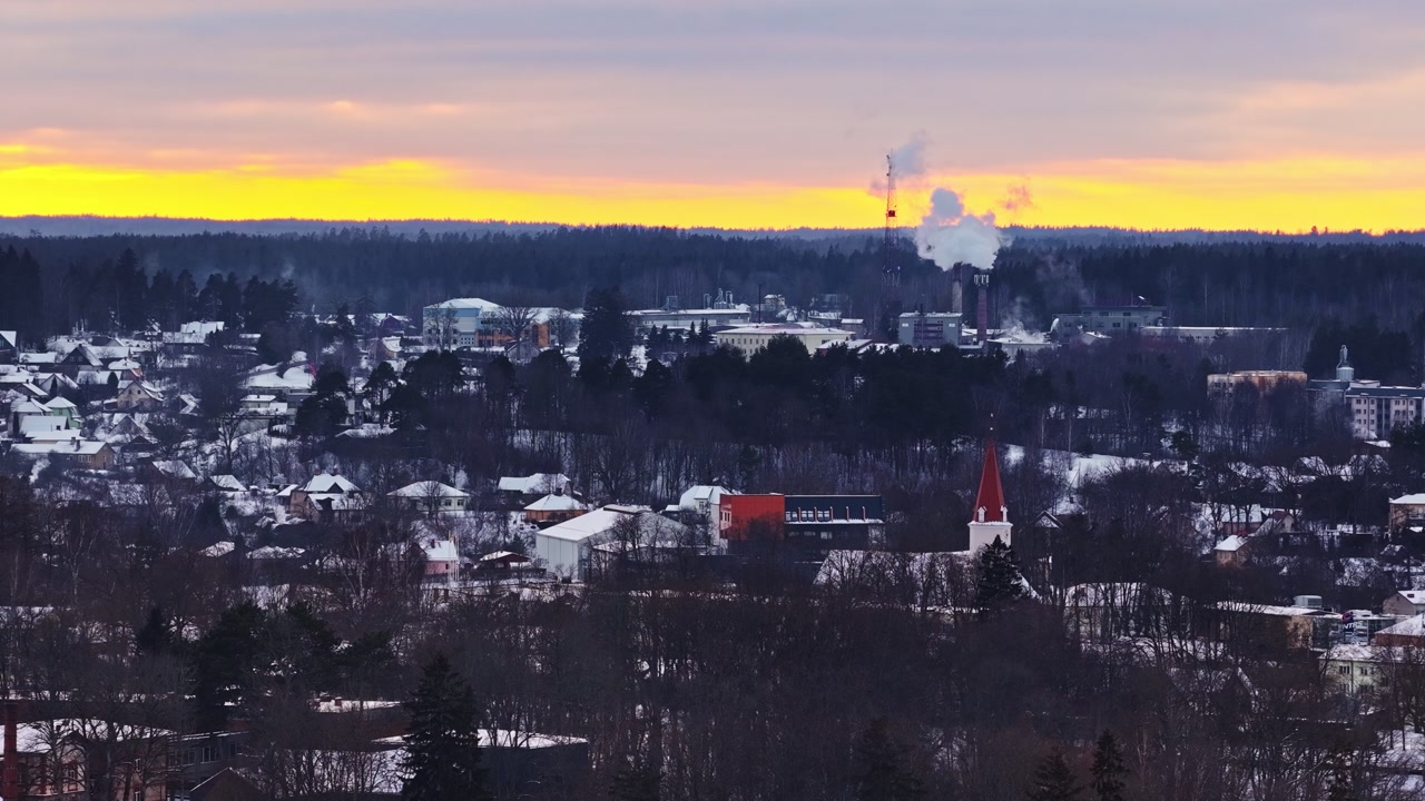 Winter town at sunset with industrial chimneys releasing vapor, aerial view