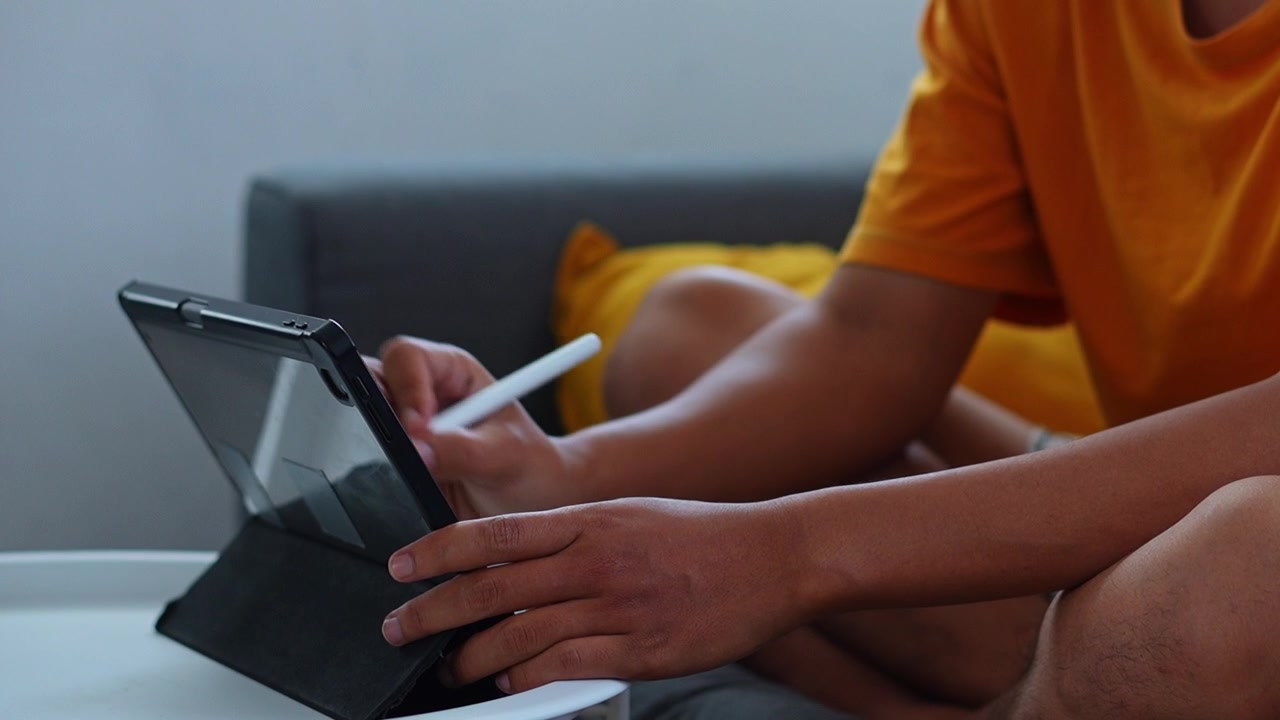 Side angle view of hands sketching on standing tablet screen while relaxing on sofa