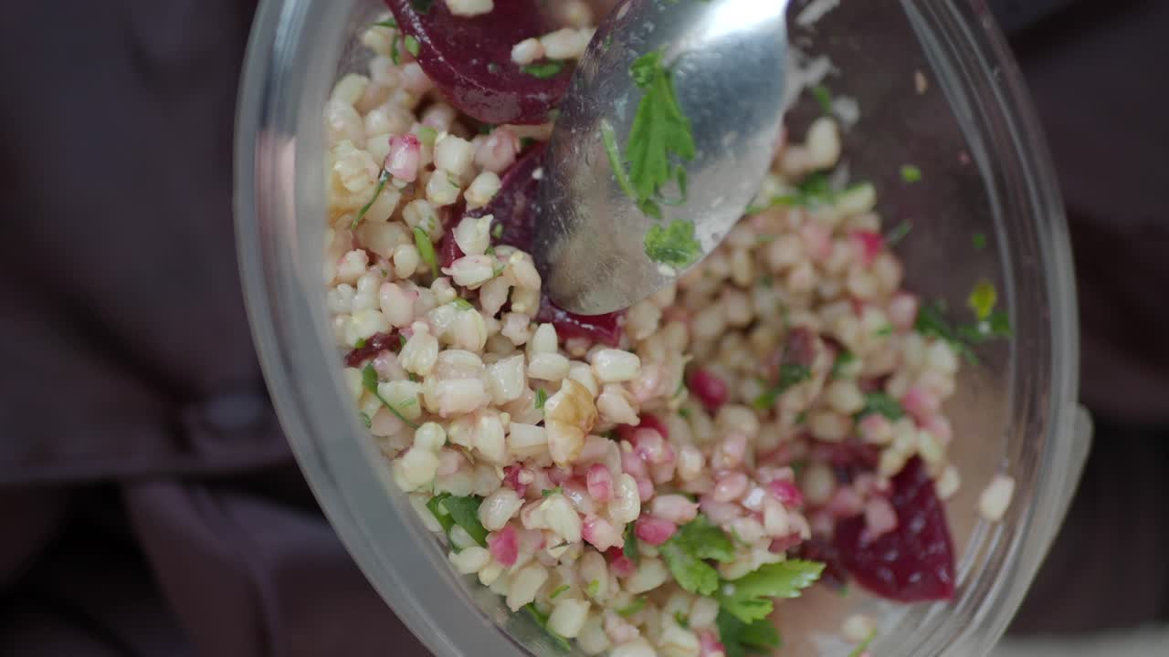 Close-up of a vibrant corn salad with herbs and red ingredients being stirred in a clear bowl