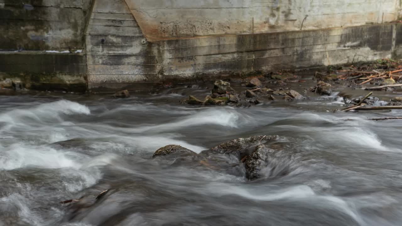 Timelapse of river current flowing over rocks along concrete dam wall