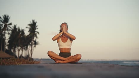 fit woman raising hands together in lotus pose prayer, breathing calmly