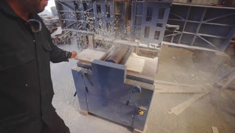 sawdust flies as woodworker uses industrial wood planer