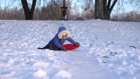 Kleines-Mädchen-Fährt-Auf-Einem-Eisschlitten-Den-Winterlich-Schneebedeckten-Hügel-Hinunter