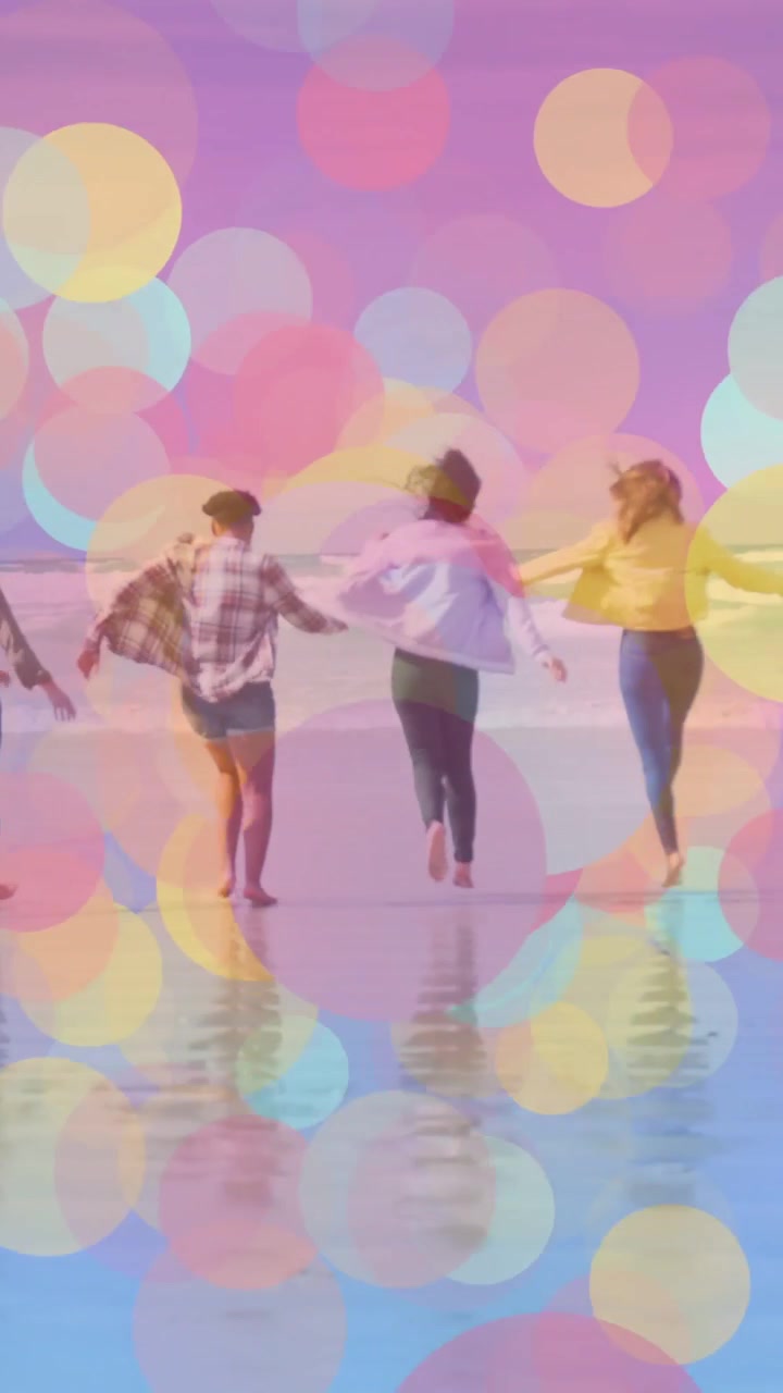 Vertical video: Four women hopping, linking and running on sand for fun, travel bokeh filling frame