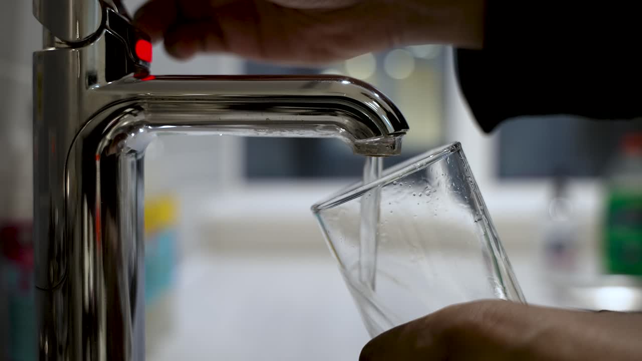 primer plano de una mano llenando un vaso transparente con agua de un grifo moderno, entorno de cocina