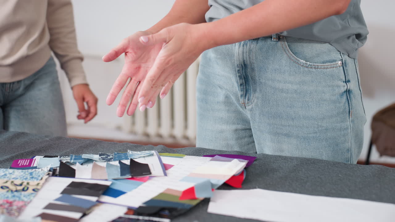 Waist view of fashion instructor wearing casual clothes showing trainee various fabric samples and material qualities during design session, emphasizing hands-on learning approach