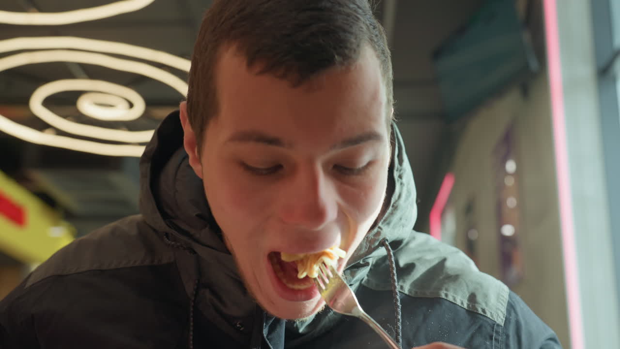 Joven blanco comiendo comida callejera bajo luces de neón en espiral con chaqueta de invierno, retrato de cerca mostrando expresión pensativa mientras prueba una cucharada, escena nocturna urbana íntima con un brillo cálido y espontáneo.