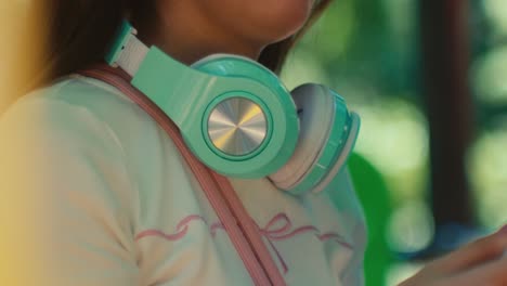 close up of green headphone on the neck of a female woman while standing outdoor waiting for a date , blurred bokeh background