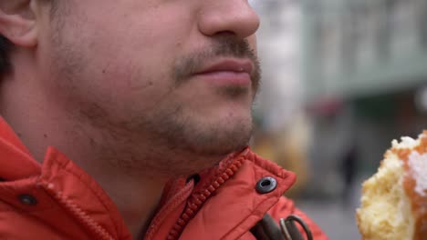 man eating traditional polish donut on city street