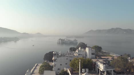 Panoramic-of-Lake-Pichola-and-Taj-Lake-Palace-from-Ambrai-Ghat-in-Udaipur,-Rajasthan,-India---Aerial-Low-angle-Orbit-shot