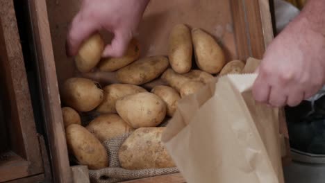 Primer-Plano-De-Recoger-Patatas-De-Una-Caja-De-Madera-Rústica-Y-Colocarlas-En-Una-Bolsa-De-Papel