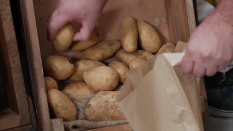 primer plano de recoger patatas de una caja rústica de madera y colocarlas en una bolsa de papel