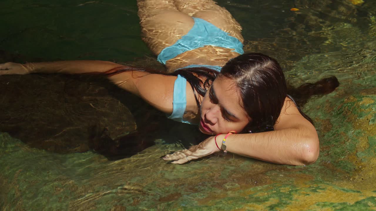 비키니 를 입은 어린 소녀 가 폭포 의  ⁇ 프 풀 의 투명 한 물 에서 수영 하고 있다